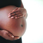 Midsection of pregnant Black woman holding belly